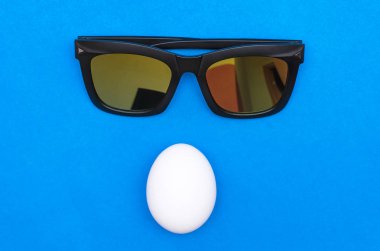 Tavuk yumurta ve izole ob mavi bir arka plan üzerinde güneş gözlüğü.