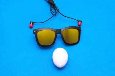 Tavuk yumurta, güneş gözlüğü ve mavi bir arka plan üzerinde kulaklık. Soyut resim.