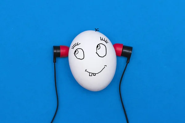 Funny chicken egg like a man head with earphones is listening a music isolated on the blue background.