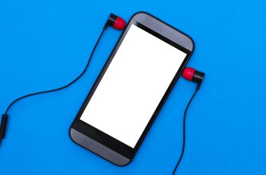 Boş ekran ve mavi bir arka plan üzerinde izole kulaklık ile cep telefonu.