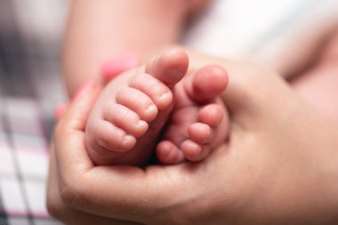 Genç anne bebeğinin küçük bir ayaklarını elele tutuyor..