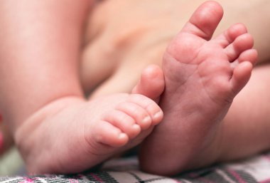 Genç anne bebeğinin küçük bir ayaklarını elele tutuyor..