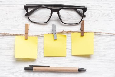 Bir ip üzerinde bir clothespin üzerinde kopya alanı ve beyaz bir masa arka plan üzerinde gözlük ile boş kağıt çıkartmalar. Yapılacaklar listesi.