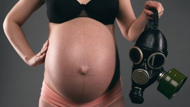 Hamile kadın gri bir arka plan üzerinde bir gaz maskesi tutuyor. Toksikoz kavramı.