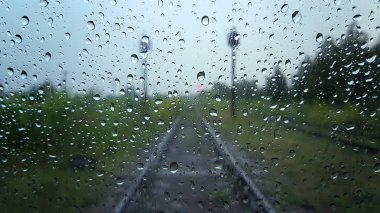 Bulanık demiryolu yolu arka planı olan bir pencerede yağmur damlaları.