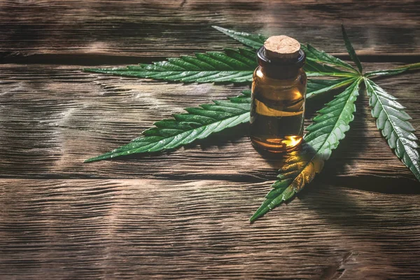 Bir kopyasını alanı ile ahşap bir masa arka plan üzerinde yeşil bir yaprak ile şişe esrar uçucu yağ. Bitkisel ilaç kavramı.