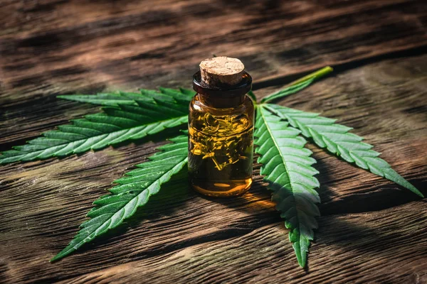 Ahşap bir tahta arka plan üzerinde yeşil bir yaprak ile şişe esrar uçucu yağ. Bitkisel ilaç kavramı.