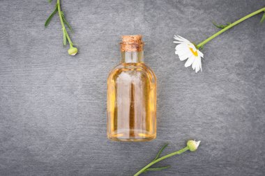 Papatya çiçeği esaslı yağ ya da aromaterapi yağı şişede ve çiçek açan gri arka planda..