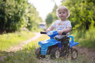 Küçük oğlan oyuncak araba dörtlü bisikleti sürüyor..