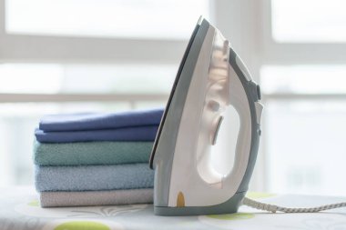 Ütü masasında elektrikli ütü ve temiz kıyafetler..