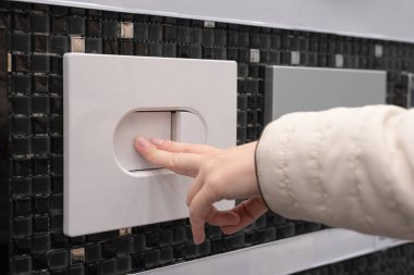 Female hand pressing a toilet flush button on the wall. clipart