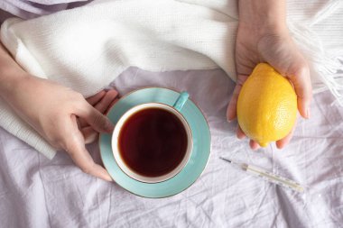 Bir fincan çay ve taze limonla yatakta hasta bir kadın..