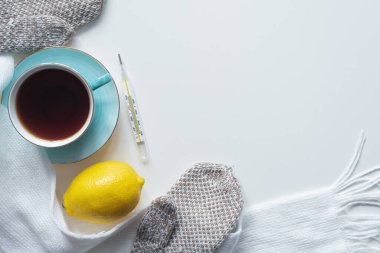 Beyaz masa üzerinde bir fincan sıcak çay, limon, termometre ve eşarp..