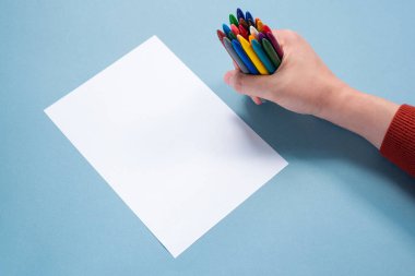 Eldeki renkli kalemler ve mavi arkaplanda kopyalama alanı olan boş kağıt sayfaları.