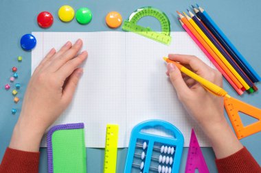 Öğrenci not defterine mavi düz zemin üzerinde kalem ve okul aksesuarlarıyla kopya alanı ile yazı yazıyor. Okul konseptine dönelim..