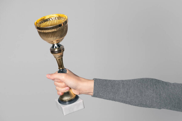 Golden award cup in winner hand isolated on gray background. Award ceremony.
