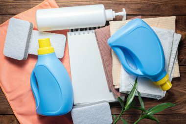 Yıkama malzemesi, yumuşatıcı, deterjan, bulaşık bezi ve ahşap masadaki boş sayfa not defteri. Ev ipuçları uydurma..