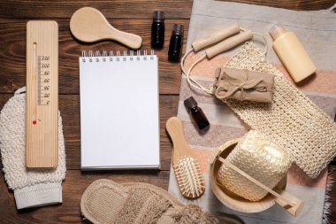 Banyo aksesuarları ve kahverengi ahşap düz arka planda fotokopi alanı olan boş bir sayfa defteri. Hijyen konsepti. Hamam ipuçları uydurma..