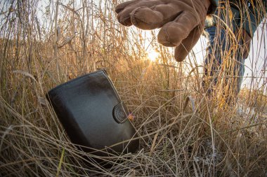 Açık havada bir çimenlikte kayıp bir cüzdan ve yerden toplayan bir kadın eli. Kapatın. Fisheye görünümü.