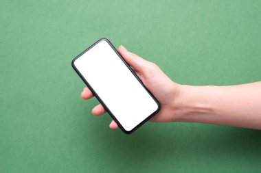 Cep telefonu, beyaz ekranlı, kadın eli yeşil arka planda. Bizimle irtibata geç..