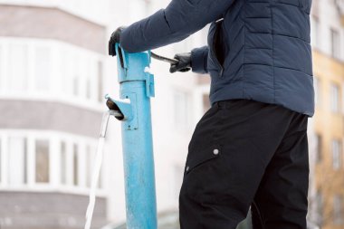 Sıcak ceketli ve pantolonlu bir adam modern bina arka planında kışın sokak sütunundan su döker..