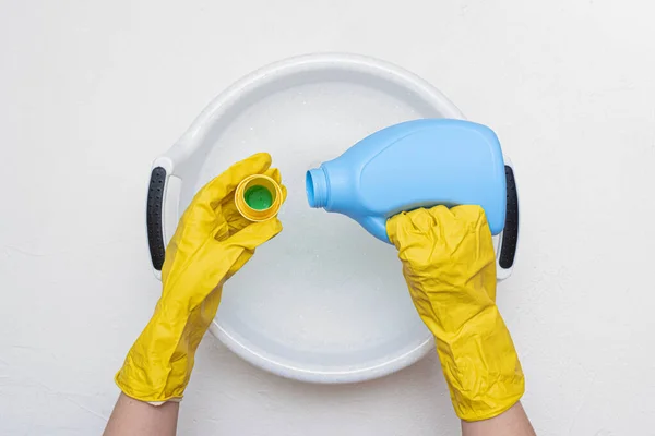 Female hands holding a wash basin with foam water flat lay background. Hand wash concept. Woman pouring a detergent in a water.