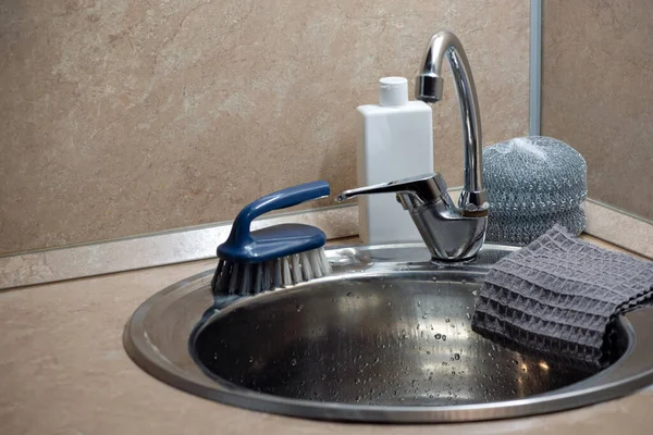 Kitchen faucet and sink with dish washing accessories close up.