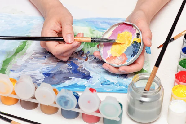 Amatör bir ressam beyaz masa arkasına guaj boyasıyla resim çiziyor..