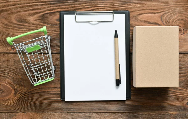 茶色のテーブルの背景にペンで郵便段ボール箱 ショッピングカート 空白のページ文書 — ストック写真