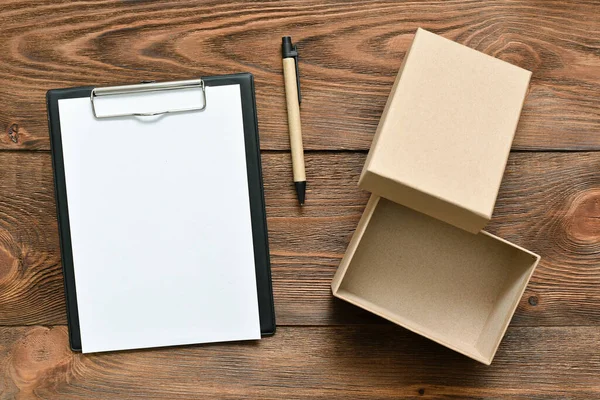 茶色のテーブルの背景にペン付きの郵便段ボール箱と空白のページ文書 — ストック写真