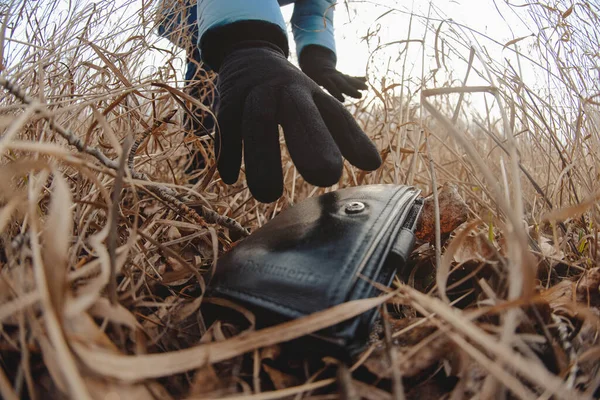 Lost wallet in a grass on the ground and female hand picking up it from a ground. Close up. Fisheye view.