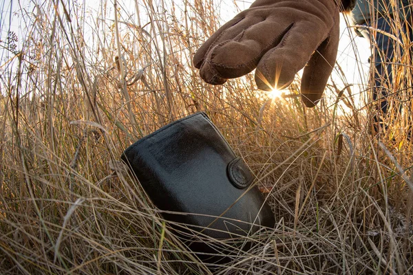 Lost wallet in a grass on the ground outdoors and female hand picking up it from a ground. Close up. Fisheye view.