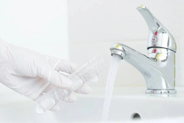 Musluk suyu analiz kalite kontrol kavramı. Elinde matara ve musluk musluğu olan bir el..