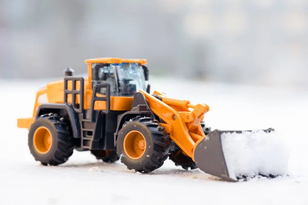 Blurred toy tractor cleaning the road from snow concept.