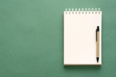 Yeşil arkaplanda boş sayfaları ve kalemi olan not defteri.