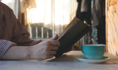 Kitap okuyan ve masanın üzerindeki fincandan çay içen bir kadın..