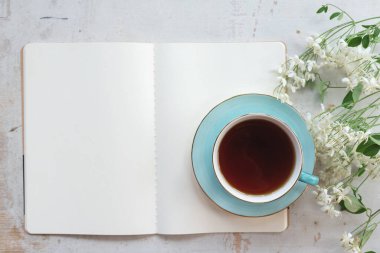 Boş bir sayfa kitabı aç. Fotokopi alanı ve beyaz ahşap bir masa üzerinde bir fincan çay..