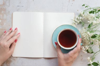 Kadın, içi boş bir sayfa kitabı okuyor ve arka planda beyaz bir masada çay içiyor..