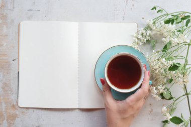 Kadın, içi boş bir sayfa kitabı okuyor ve arka planda beyaz bir masada çay içiyor..