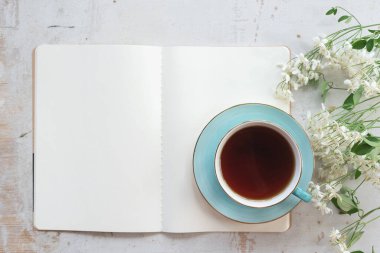 Boş bir sayfa kitabı aç. Fotokopi alanı ve beyaz ahşap bir masa üzerinde bir fincan çay..