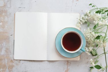 Boş bir sayfa kitabı aç. Fotokopi alanı ve beyaz ahşap bir masa üzerinde bir fincan çay..