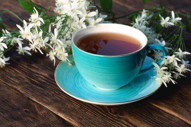 Kahverengi ahşap bir arka planda bir fincan sıcak çay ve çiçek..