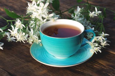 Kahverengi ahşap bir arka planda bir fincan sıcak çay ve çiçek..