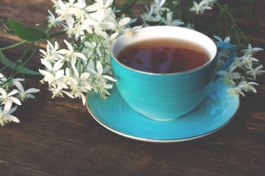 Kahverengi ahşap bir arka planda bir fincan sıcak çay ve çiçek..