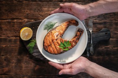 Izgara somon bifteği bir tabakta kesme tahtasının üzerinde bir erkeğin ellerinde..