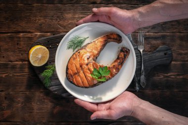 Izgara somon bifteği bir tabakta kesme tahtasının üzerinde bir erkeğin ellerinde..