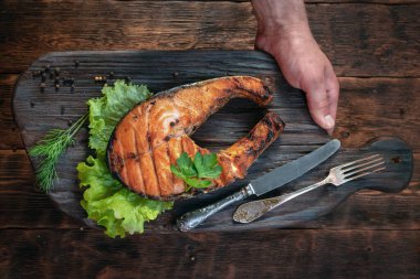 Izgara somon bifteği kesme tahtasında bir erkeğin ellerinde..
