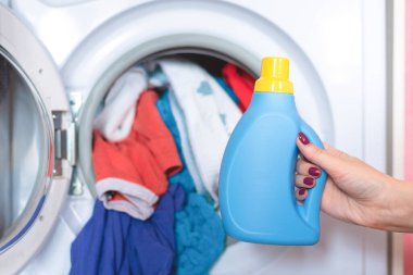 Kadın el ele çamaşır makinesinin arka planında sıvı çamaşır deterjanı tutuyor..