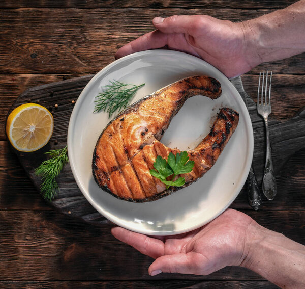 Grilled salmon steak in a plate on a cutting board in a male hands.