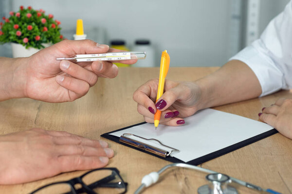 Patient with a high body temperature is giving a thermometer to a physician.